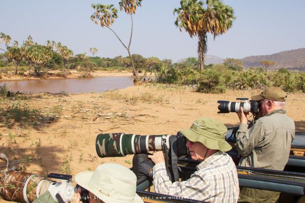 Wildlife photographers capturing river scenes from safari vehicle along Samburu’s palm-lined banks